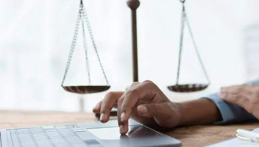 Lawyer using a laptop beside brass scales of justice