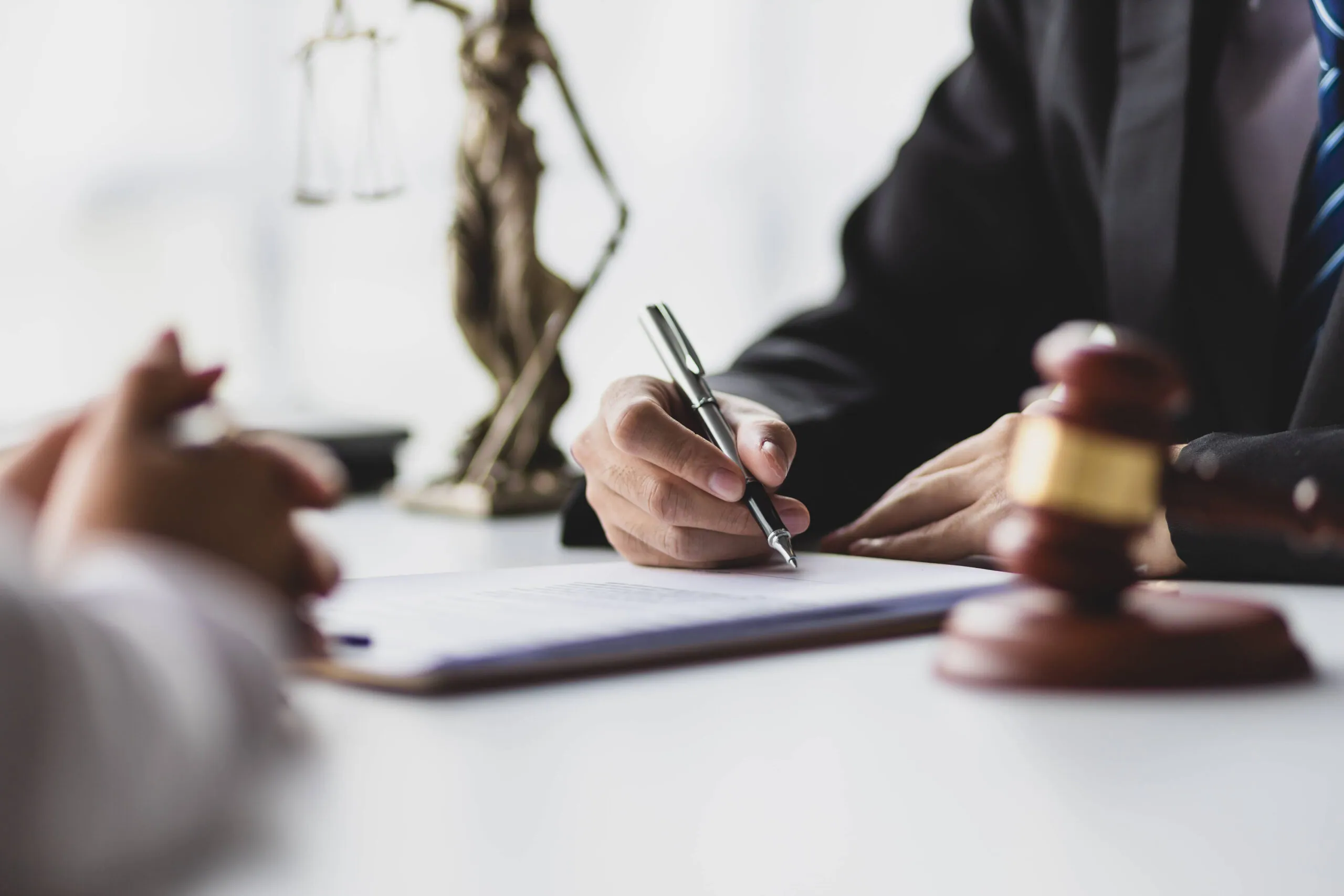Lawyer signing legal documents beside a gavel and statue of Justice