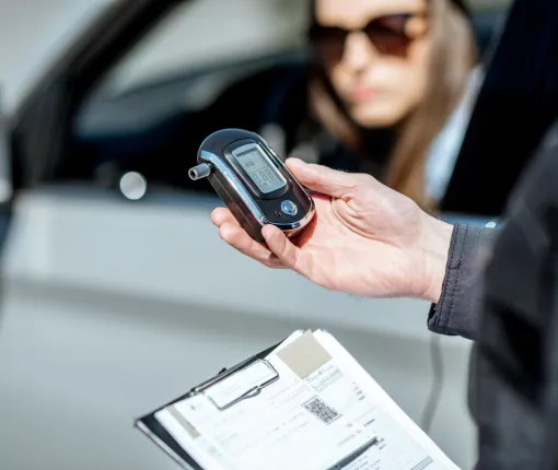 Police officer holding a breath-testing device beside a driver