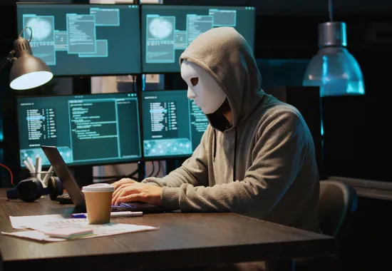 Masked person at a computer committing online fraud