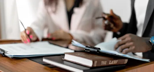Two lawyers reviewing documents at a desk with a law book