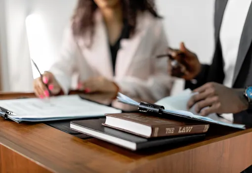 Two lawyers reviewing documents at a desk with a law book