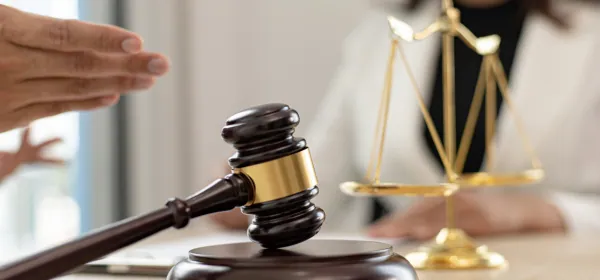 Lawyer gesturing across a desk with a gavel and scales in front