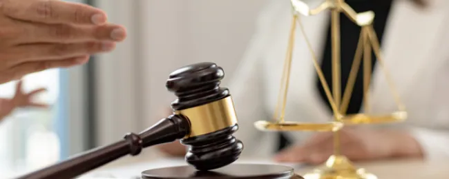 Lawyer gesturing across a desk with a gavel and scales in front