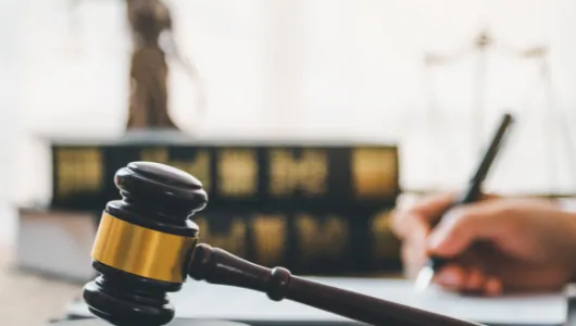 Gavel resting on a desk in front of law books and a statue of Justice