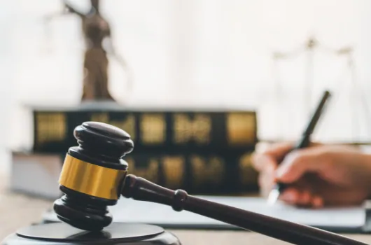 Gavel resting on a desk in front of law books and a statue of Justice