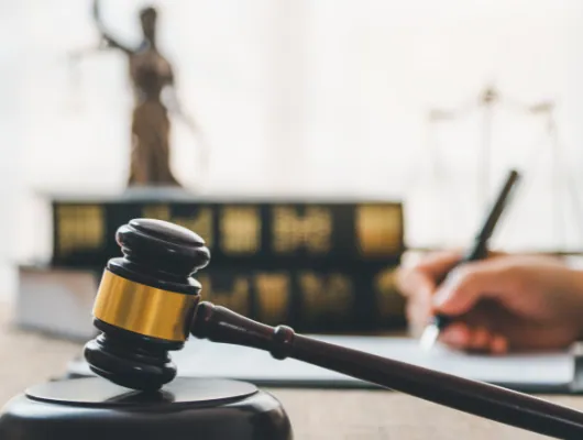 Gavel resting on a desk in front of law books and a statue of Justice
