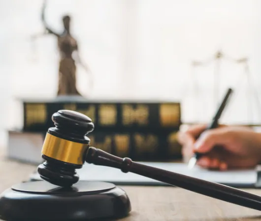 Gavel resting on a desk in front of law books and a statue of Justice