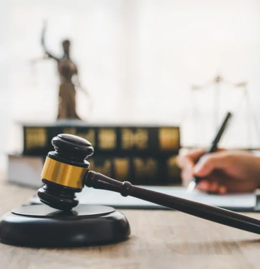 Gavel resting on a desk in front of law books and a statue of Justice