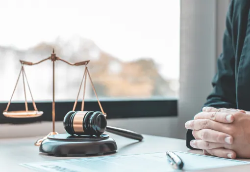 Scales of justice and a gavel on a desk beside a seated client